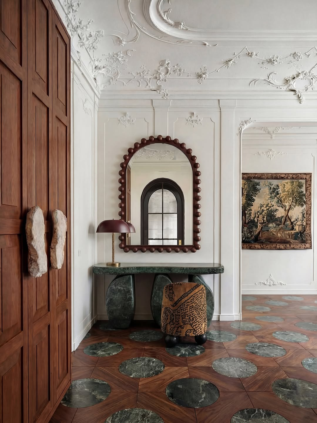 Sculptural entryway with ornate ceiling details, green marble console table, statement mirror and patterned flooring blending classic and modern design trends 2026