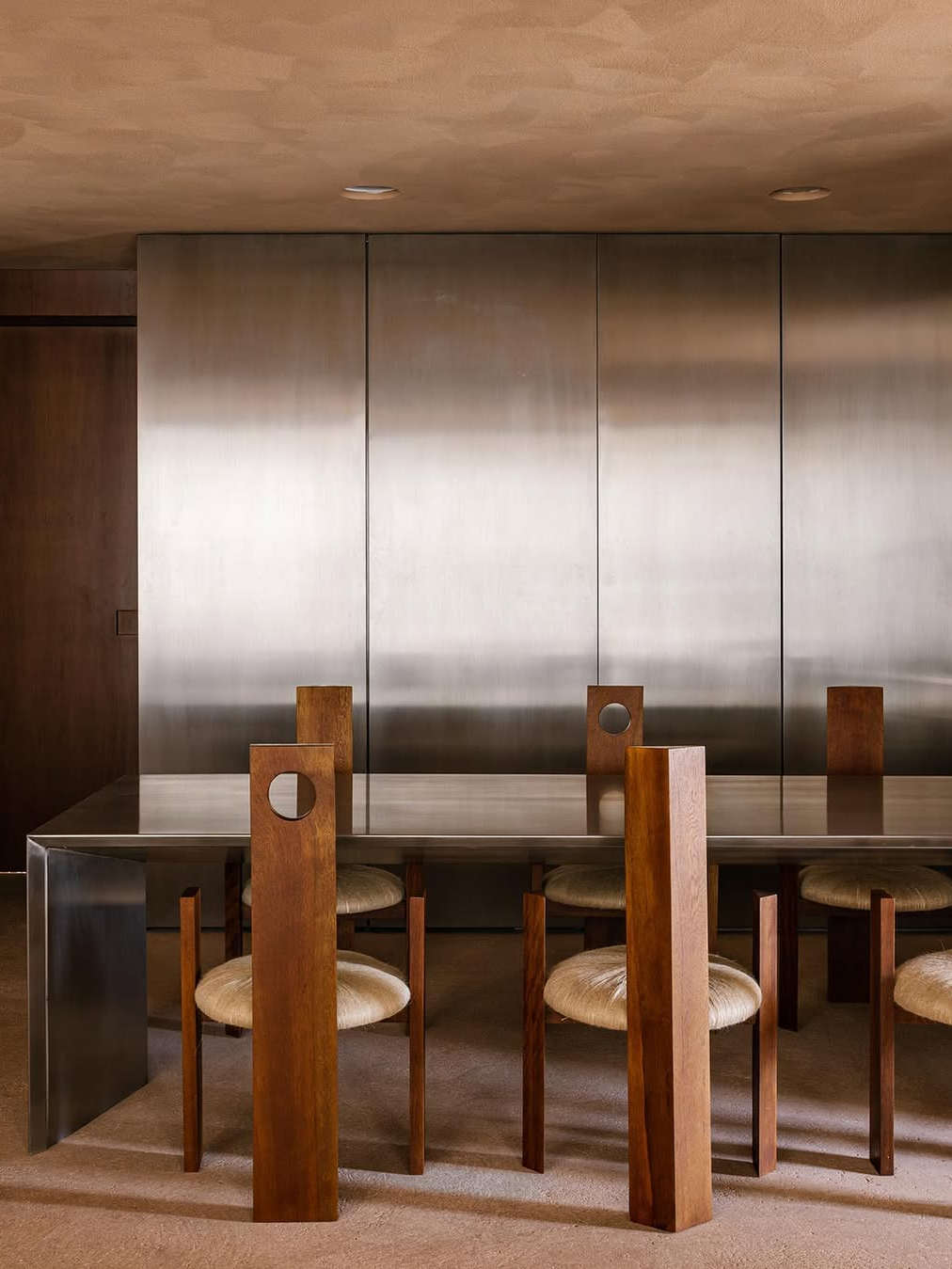 Minimal sculptural dining room with architectural wood chairs, metal table and warm neutral tones reflecting modern interior design trends 2026
